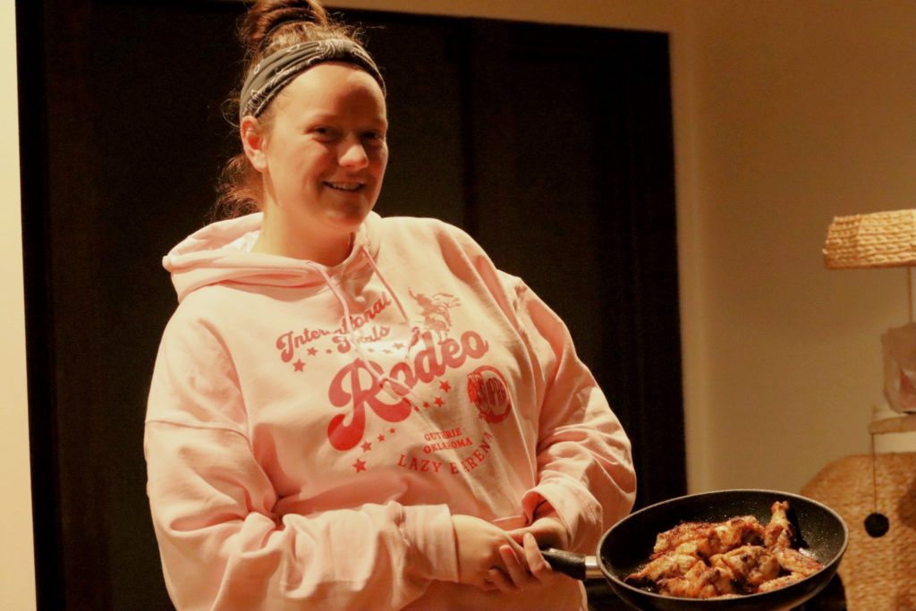 A person stands holding a pan with cooked chicken as part of a dinner scene.